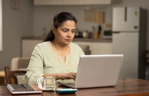 Woman working on laptop at wooden kitchen table
