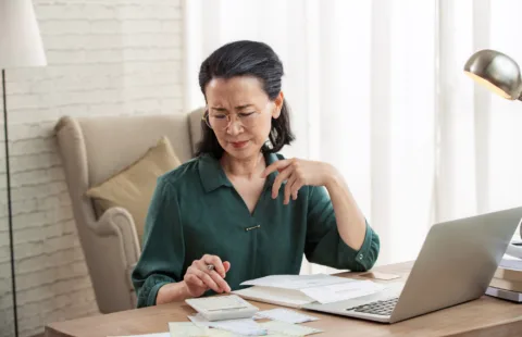 Woman reviewing financial documents at home office desk with laptop
