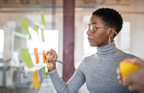 Woman writing on colorful sticky notes on glass wall in bright office